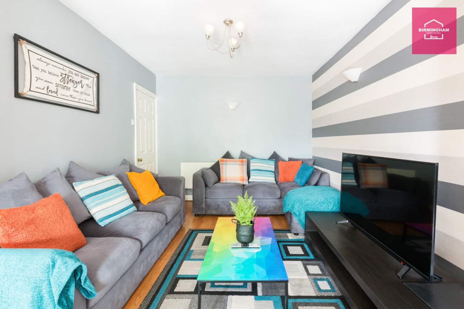 Vibrantly decorated living room with comfortable sofas, colorful pillows, and a modern coffee table. A large TV is mounted on the wall. This inviting space is a contractor house for rent in Birmingham, featuring 4 bedrooms that can accommodate up to 7 guests