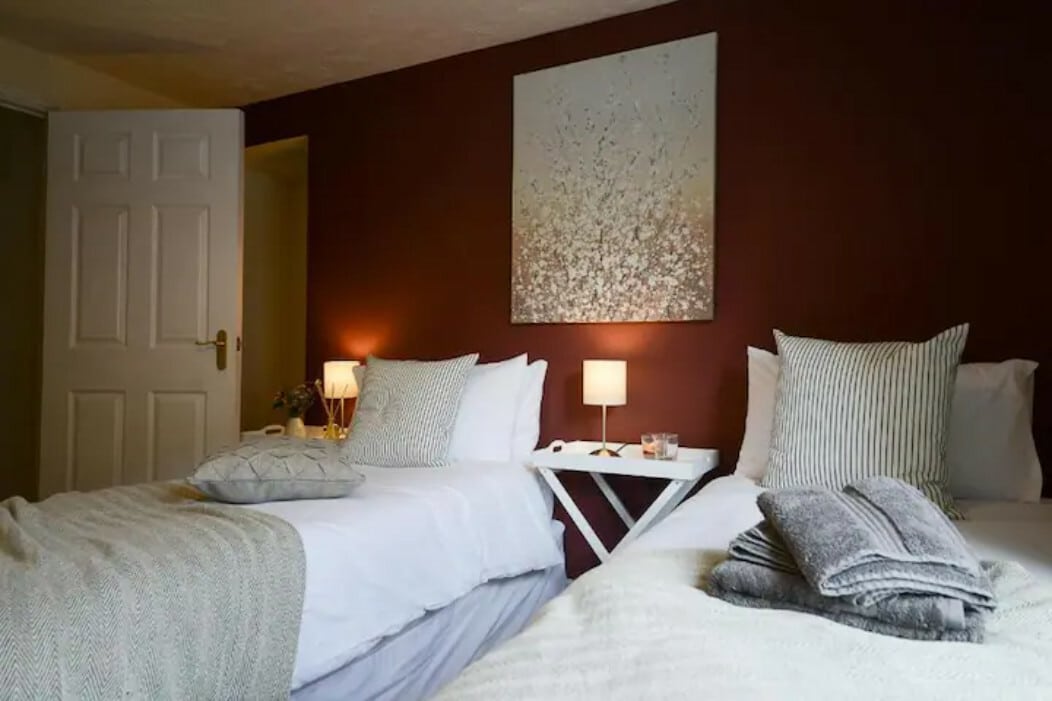 Cosy bedroom with two beds, white linens, and stylish decor. A large artwork hangs on the wall. This apartment is a comfortable Solihull accommodation.